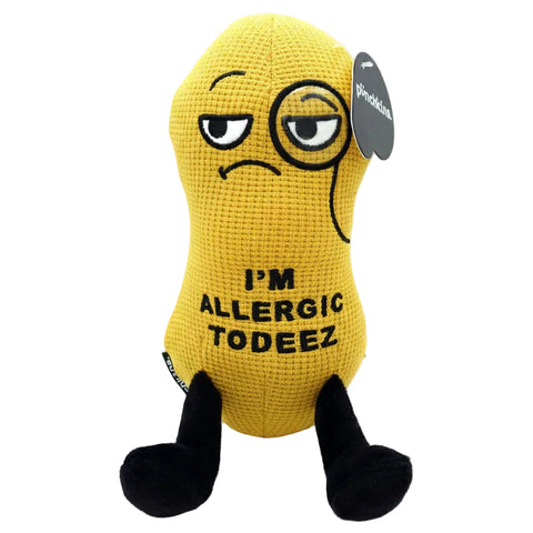 A yellow crocheted plush toy shaped like a peanut with black legs and a sad face, featuring the text 'I'M ALLERGIC TO DEEZ' and a small side tag.